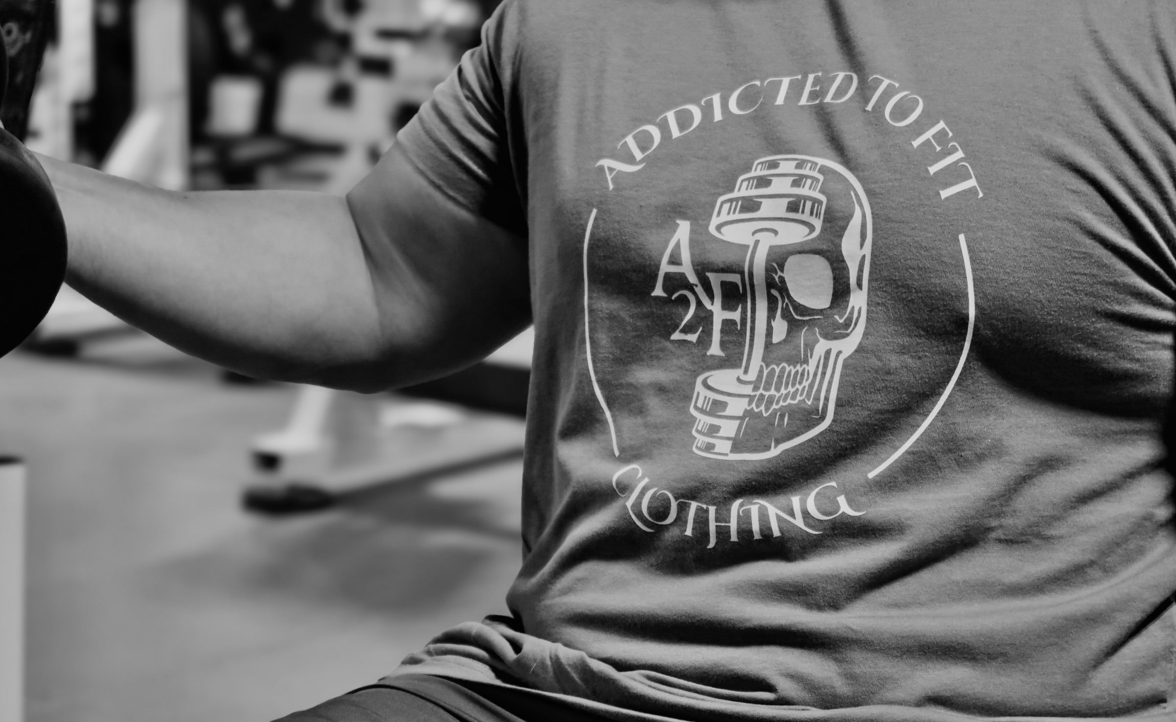Black and white photo of a person wearing an 'Addicted to Fitness' shirt with a skull and helmet design.